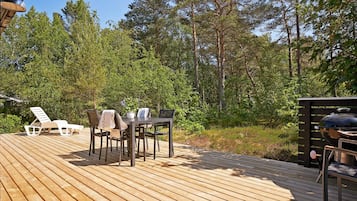 Una terraza de madera con mobiliario exterior, rodeada de árboles.