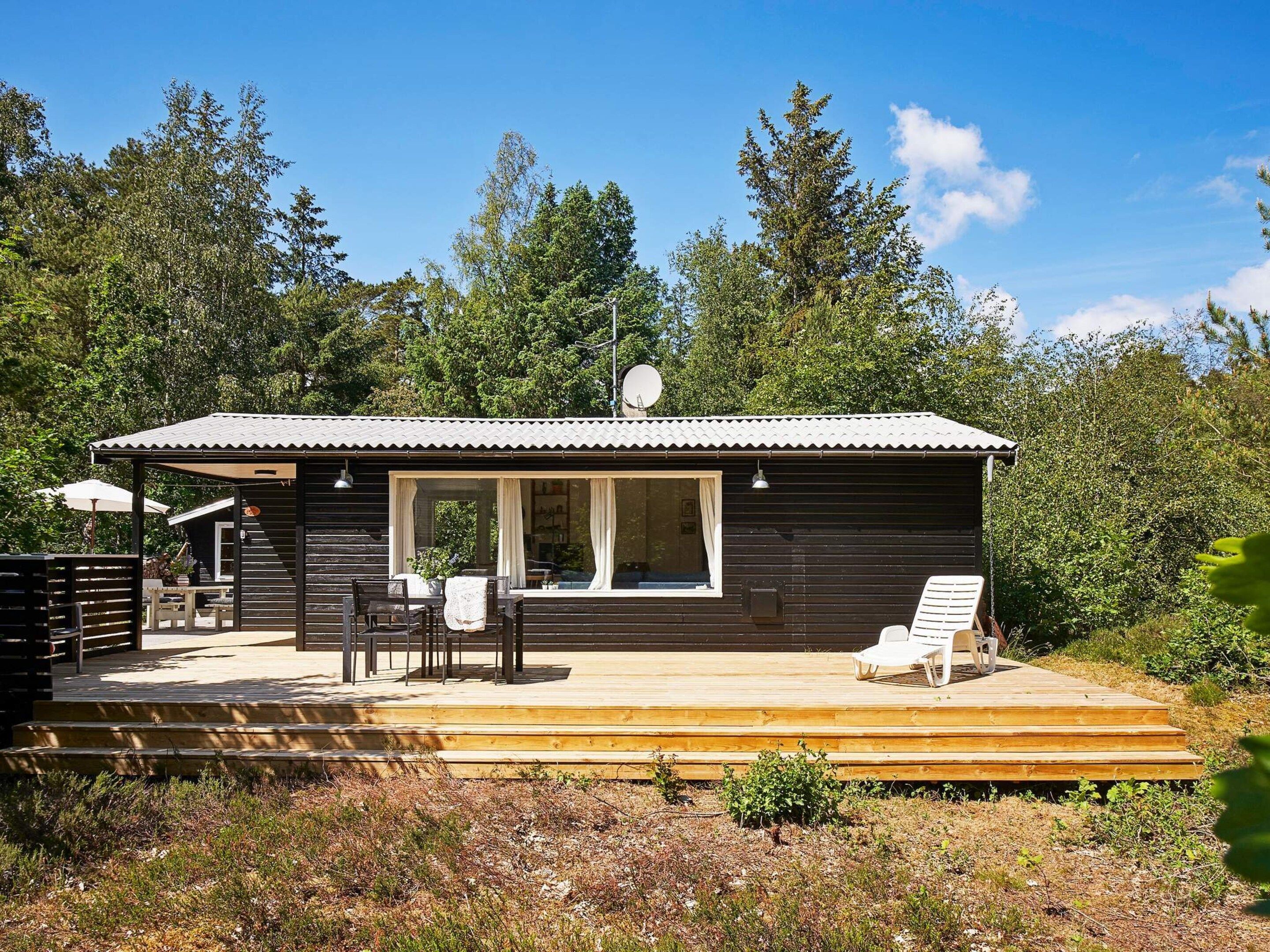 En træhytte med terrasse, udendørs møbler og parabol.