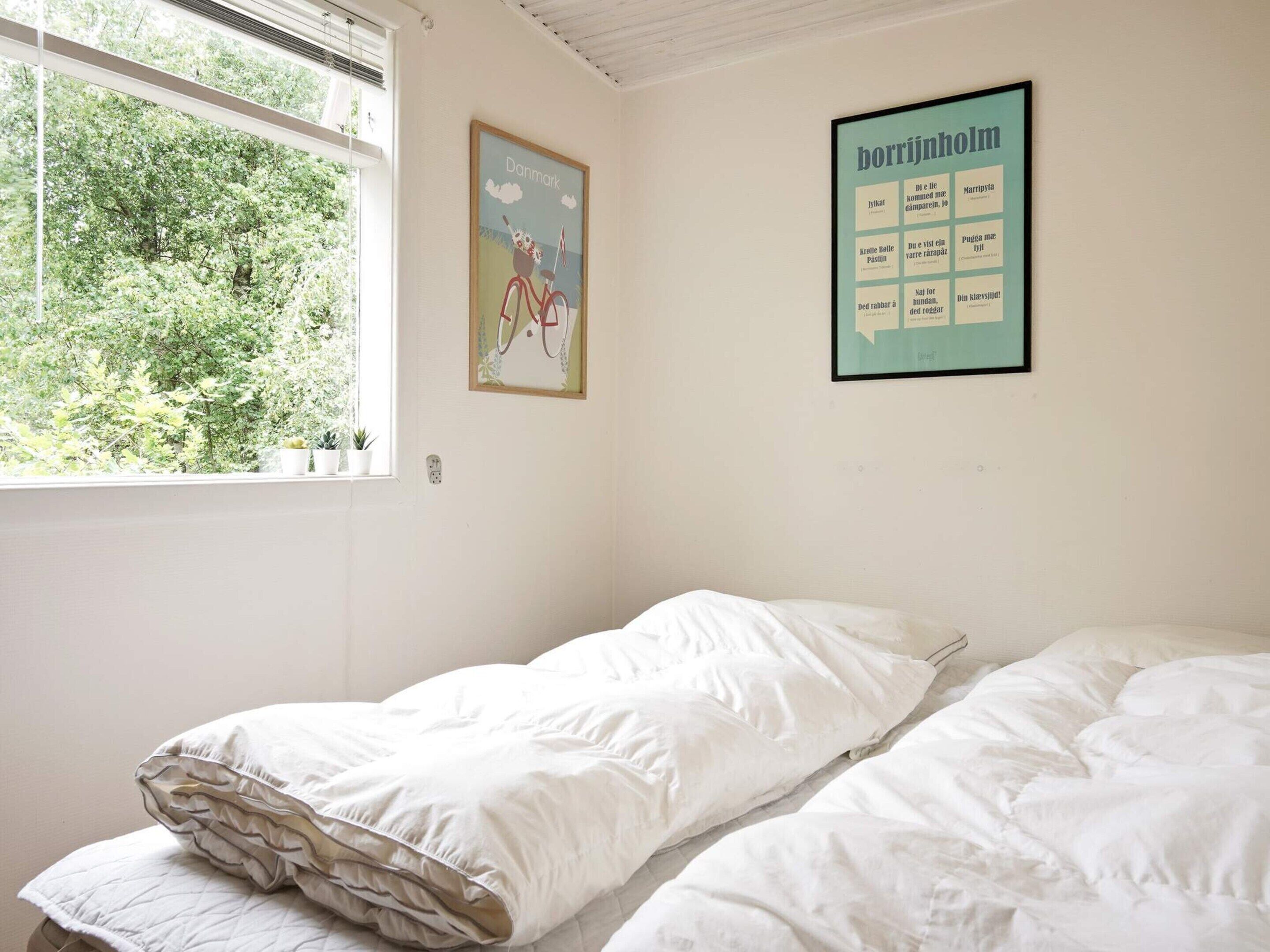 A single-bed room with a window, a wall poster, and a wall-mounted sign.
