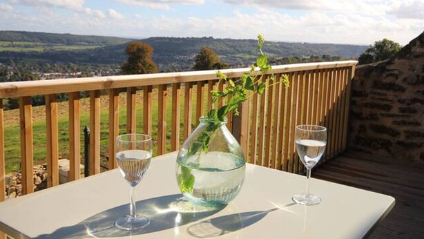 A table with two wine glasses and a vase on a deck overlooking a scenic landscape. - Stunning cottage close to city centre - Pass the Keys (Bath)