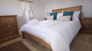 A neatly made bed with white linens and teal pillows, a wooden nightstand with a lamp, and a wooden dresser with drawers. - Stunning location close to city centre - Pass the Keys (Bath)