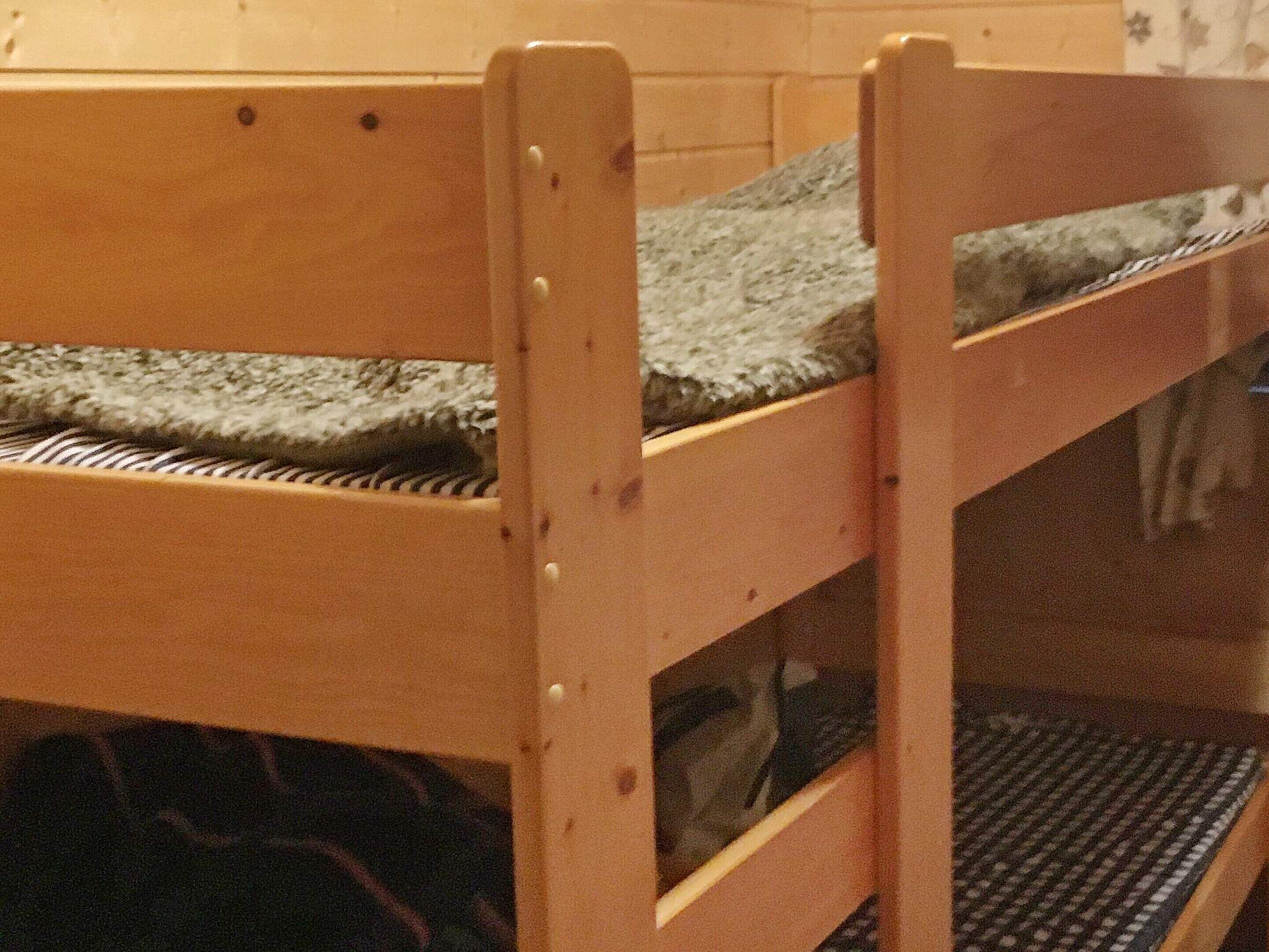 Un lit superposé avec une structure en bois et un matelas gris.
