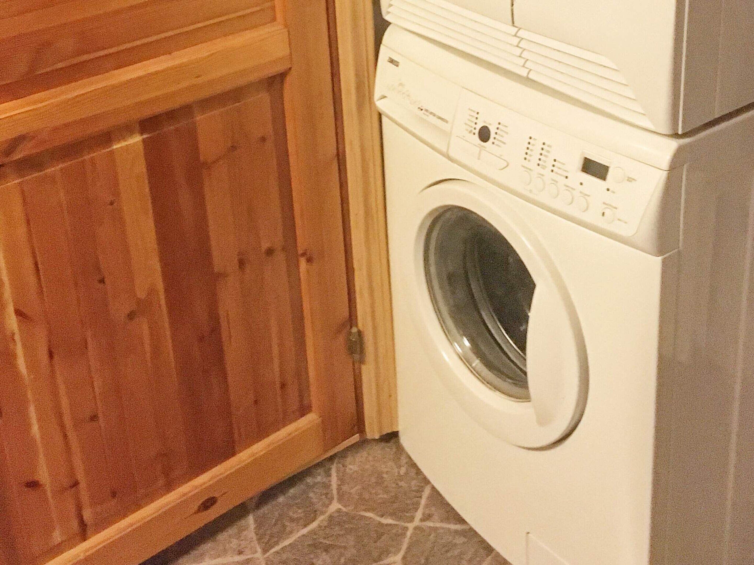 Una sala de bugaderia amb una rentadora de càrrega frontal i un armari de fusta.
