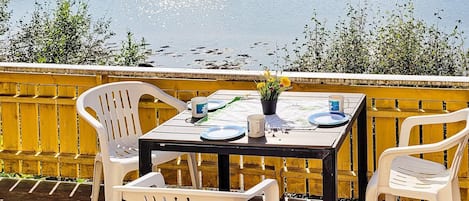 Ein Tisch für zwei Personen, mit weißen Plastikstühlen, einer kleinen Tischplatte und einem Blumentopf mit gelben Blüten.
