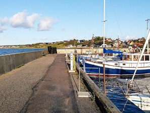 A coastal marina with boats docked, a concrete walkway, and houses in the background.