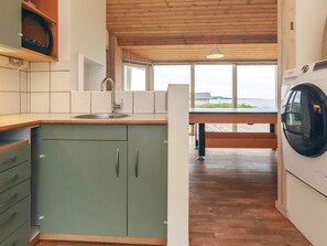 A kitchen with a wooden ceiling, a built-in washing machine, and a view of the outdoors through large windows.