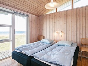 A bedroom with two beds, a window with a view of the beach, and a wooden ceiling.