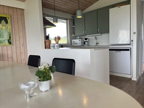 A modern kitchen with a dining area, featuring a central island, a microwave, a coffee maker, and wooden cabinets. - 10 Person Holiday Home in Farso (Farso)