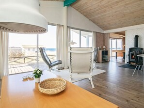 A modern interior with a wooden floor, a white chair, a table with a woven basket, and a fireplace. - 10 Person Holiday Home in Farso (Farso)