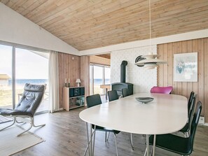 A modern interior with a dining area, a sofa, a fireplace, and a view of the sea.