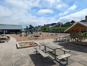 A playground with swings, a slide, and picnic tables. - 10 Person Holiday Home in Farso (Farso)