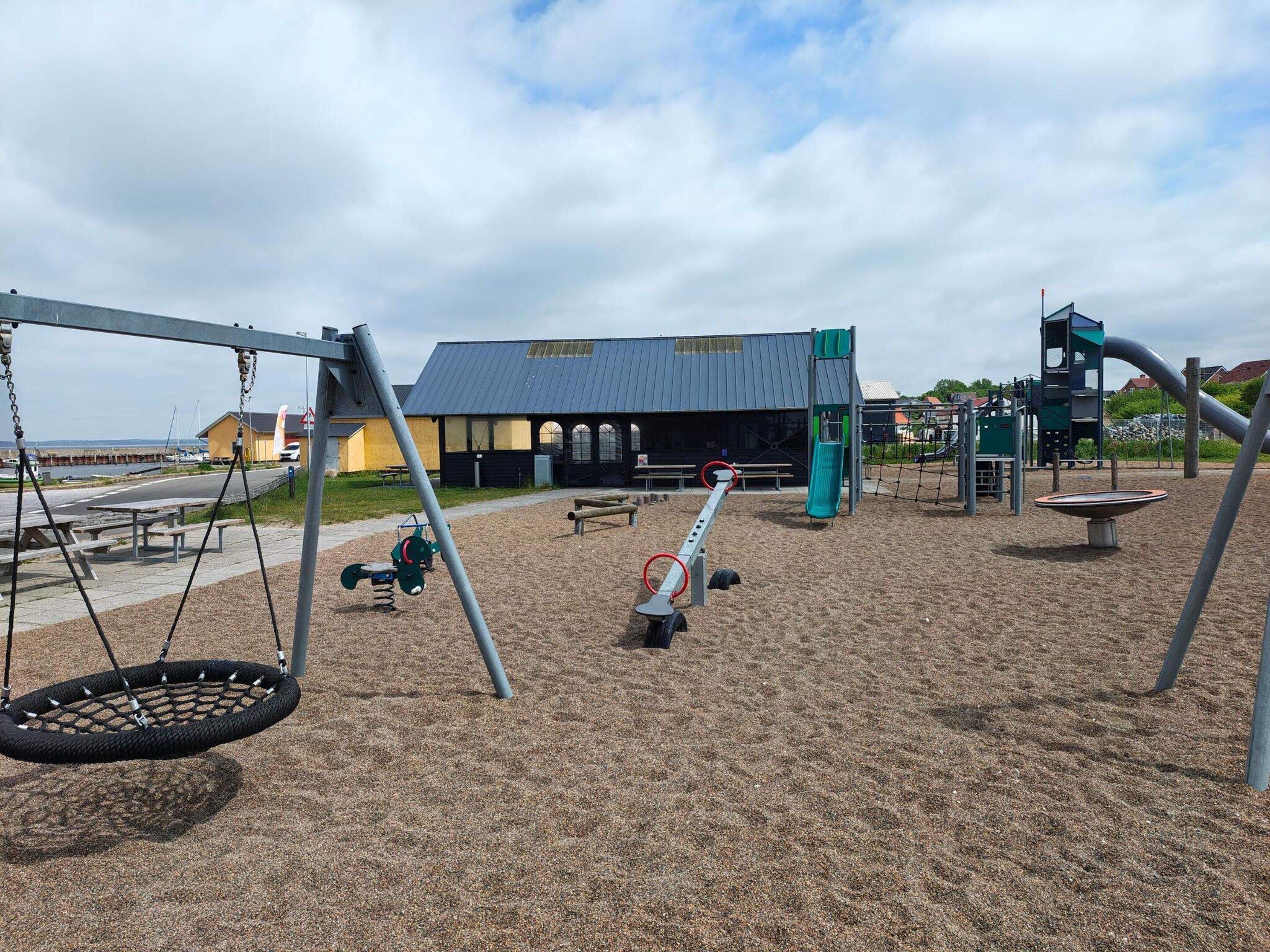 A playground with swings, a seesaw, and a slide.