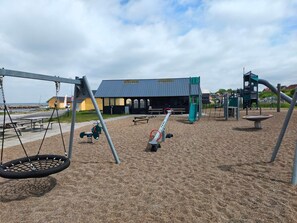 A playground with swings, a seesaw, and a slide. - 10 Person Holiday Home in Farso (Farso)