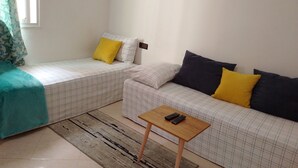 A small, clean room with two beds, a sofa, a wooden table, and a window with curtains.