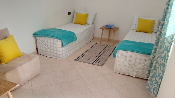 A small, clean room with two beds, a wooden table, and a small stool.