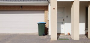 garage with a closed door and adjacent trash bin on a paved driveway.