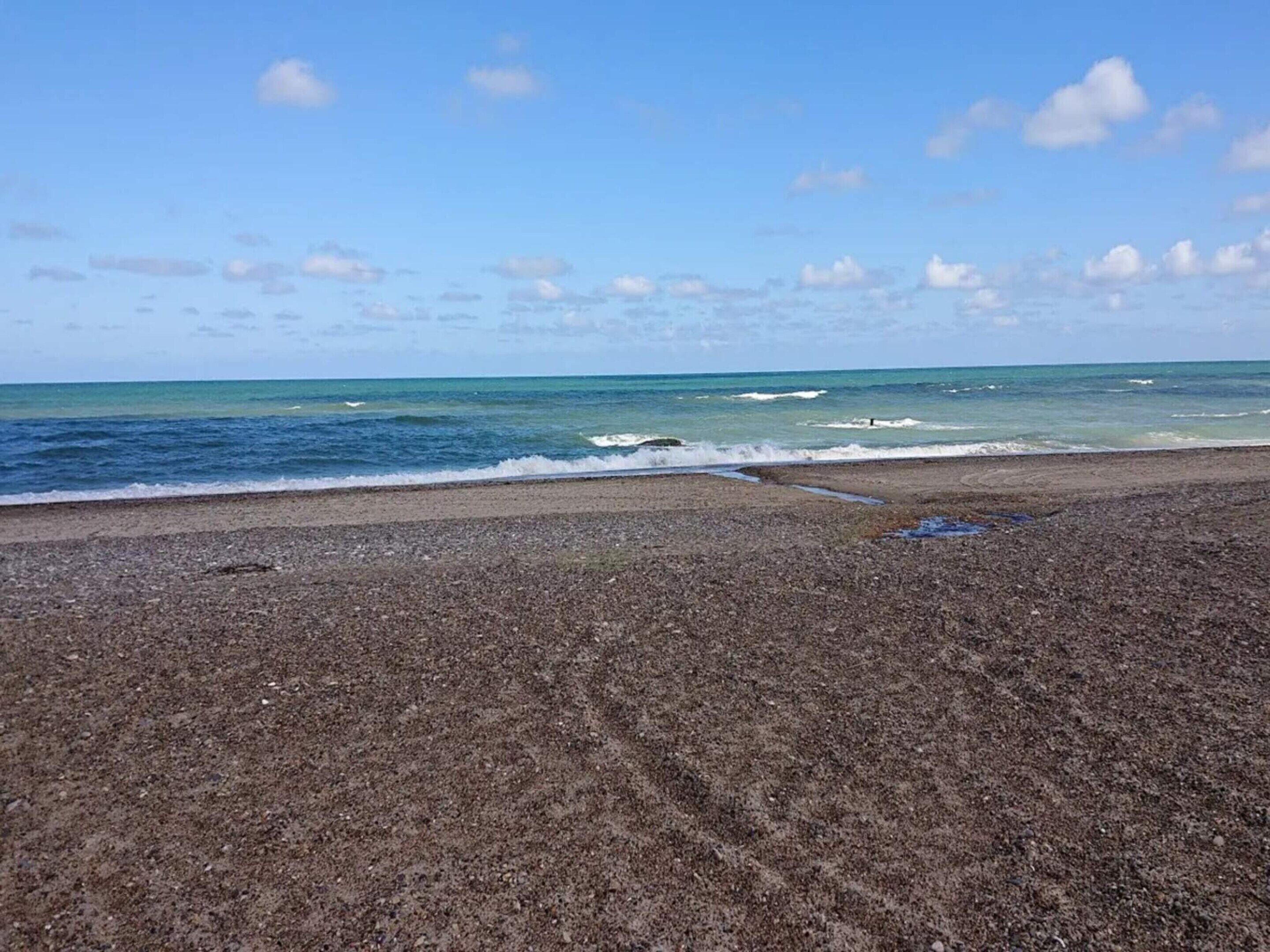 Een kiezelstrand met een helder uitzicht op de oceaan en een gedeeltelijk bewolkte lucht.