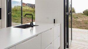 A modern kitchen with a black faucet, white cabinets, and a view of a garden through a glass door. - 8 Person Holiday Home in Ebeltoft (Ebeltoft)