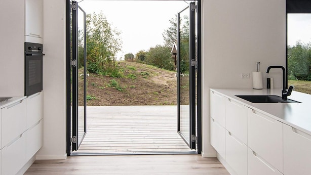 A modern kitchen with an open door leading to a wooden deck and garden. - 8 Person Holiday Home in Ebeltoft (Ebeltoft)