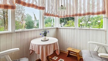 A cozy corner with a round table, two chairs, a small stool, and a view of greenery outside.