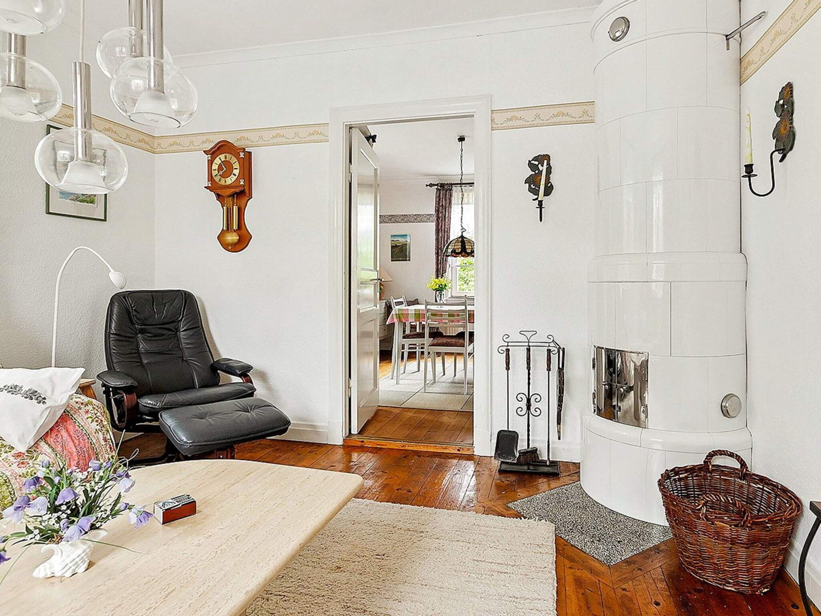 Una habitación con una butaca de cuero negro, una chimenea blanca y un comedor visible a través de una puerta abierta.