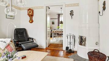 Una habitación con una butaca de cuero negro, una chimenea blanca y un comedor visible a través de una puerta abierta.