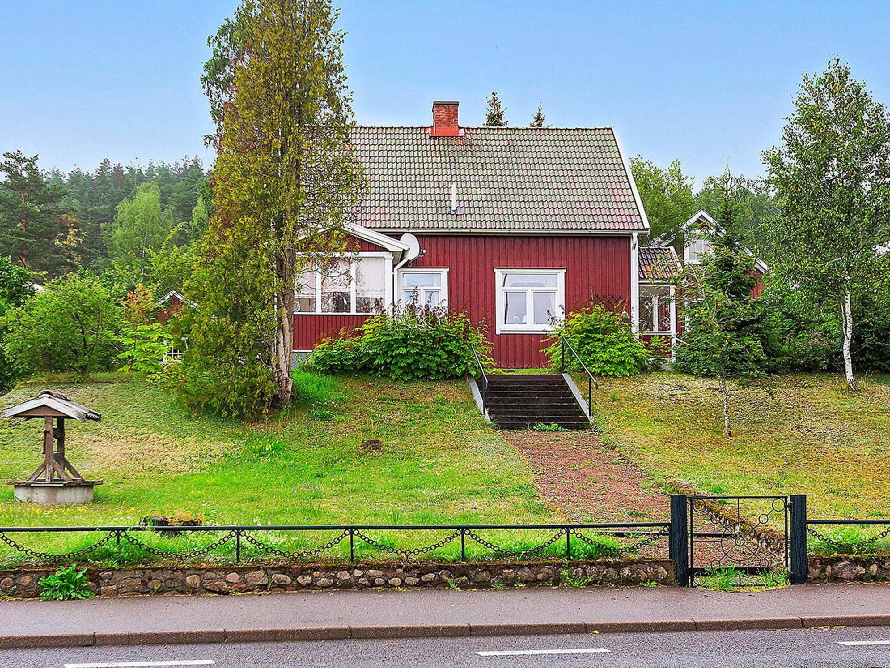 Une maison rouge avec un toit en pente, un porche à l’avant et un petit jardin devant, agrémenté d’une statue et d’une clôture.