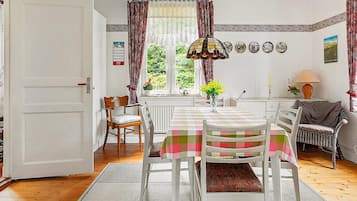 A dining area with a table set for four, surrounded by chairs, a hanging light fixture, and a view of greenery outside.