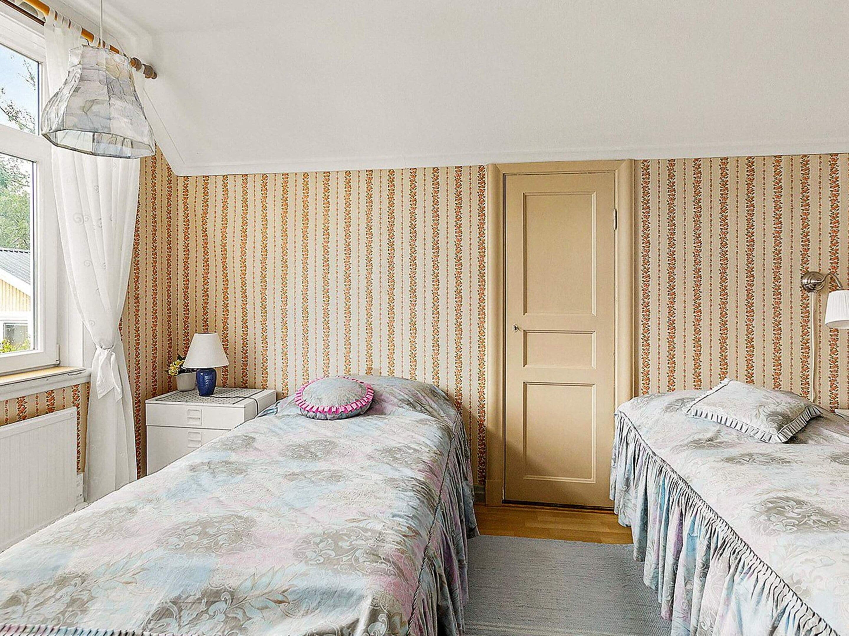 Un dormitorio con dos camas, una mesita de noche, una lámpara, una ventana con cortinas y una puerta.