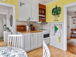 A kitchen with white cabinets, a wooden countertop, and a stove. There is a dining table with chairs and a decorative wall hanging.