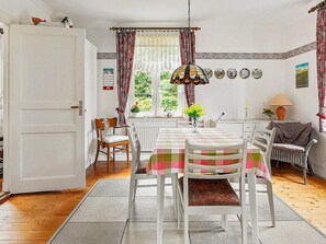 En matplats med ett bord dukat för fyra personer, ett fönster med gardiner och utsikt över grönskan utanför.