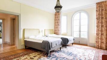 A spacious bedroom with two beds, a large window, and a traditional chandelier.
