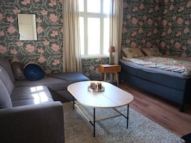 Una habitación con sofá, una mesita con bandeja, lámpara y cama con ropa de cama estampada.