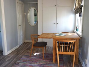 A small dining area with a wooden table, two chairs, a colorful rug, and a window with blinds. - 4 Person Holiday Home in Ronneby (Ronneby)