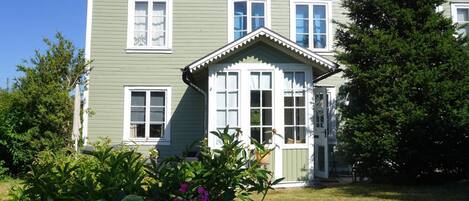 Ein zweistöckiges Haus mit grüner Fassade, weißen Verzierungen und zahlreichen Fenstern.
