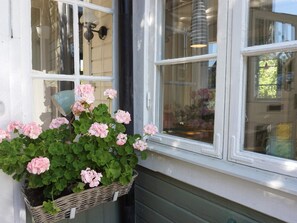 Een raam met een rieten mand vol roze bloemen, een hanglamp en een uitzicht op een gebouw.