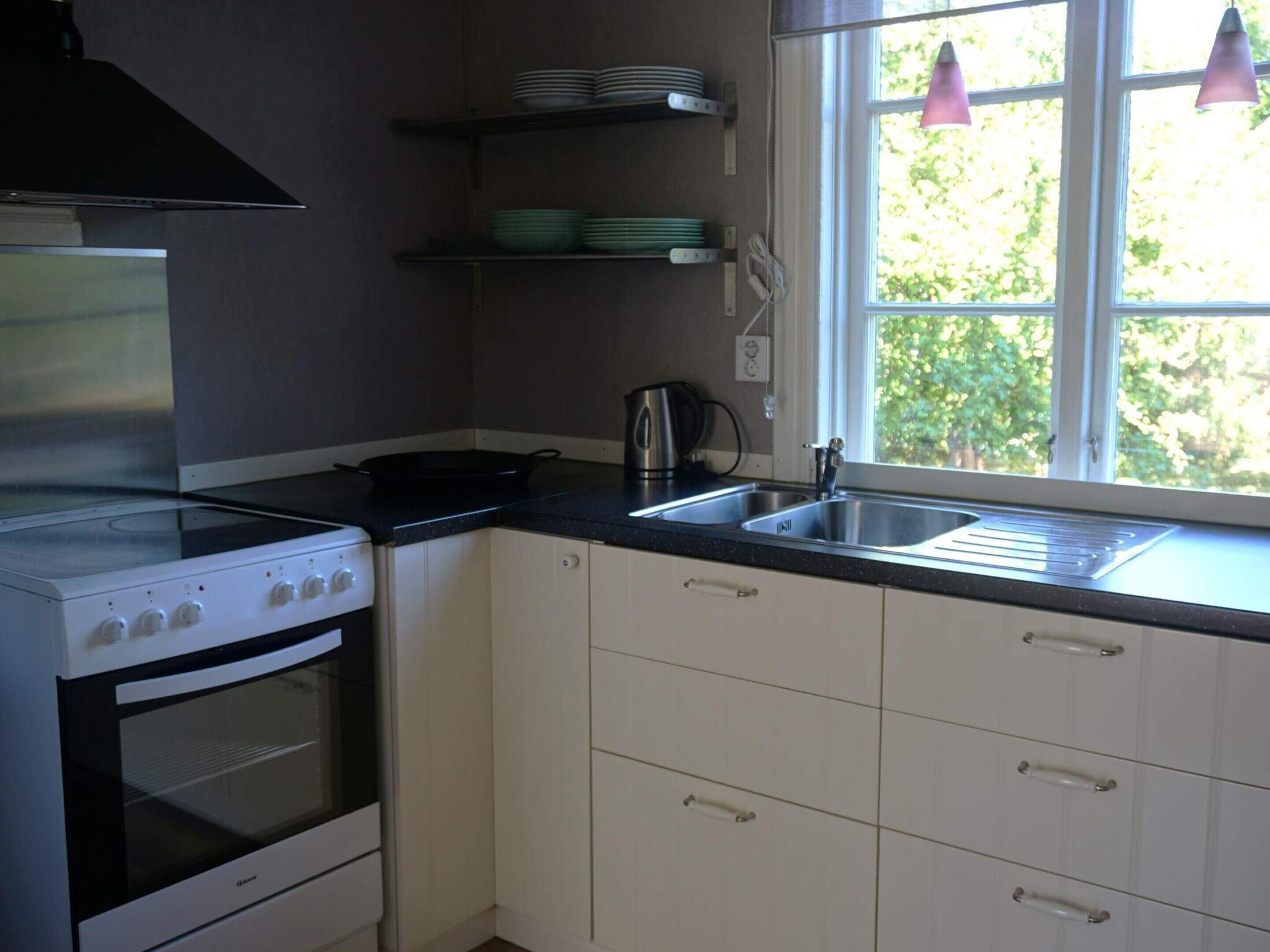 Una cocina equipada con estufa, horno, lavaplatos y ventana con cortinas.