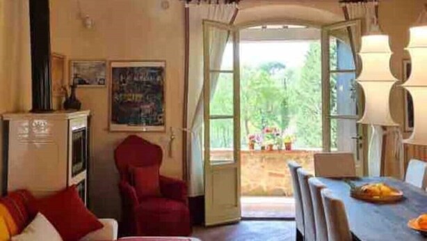 A cozy room with a wooden ceiling, a patterned rug, a sofa, a red armchair, and a dining area with a table and chairs. - Villa under the Tuscan sun (Toscana)