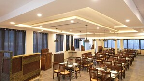 Un comedor amplio con varias mesas y sillas, un mostrador de recepción y ventanas grandes con cortinas.