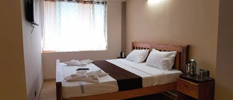 A neatly made bed with a wooden headboard, a bedside table with a lamp, and a window with sheer curtains.