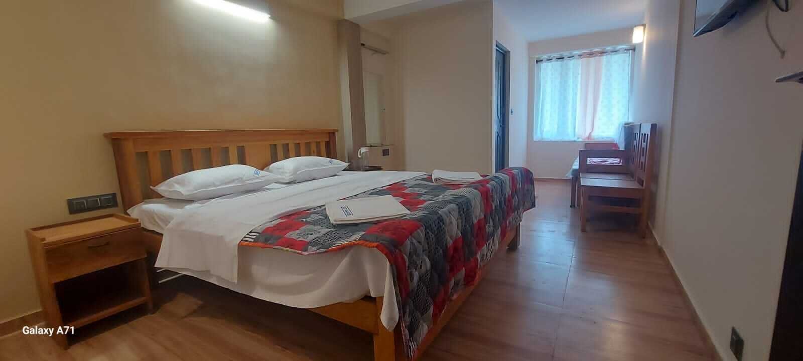 A bedroom with a wooden bed, a bedside table, a desk, and a chair.