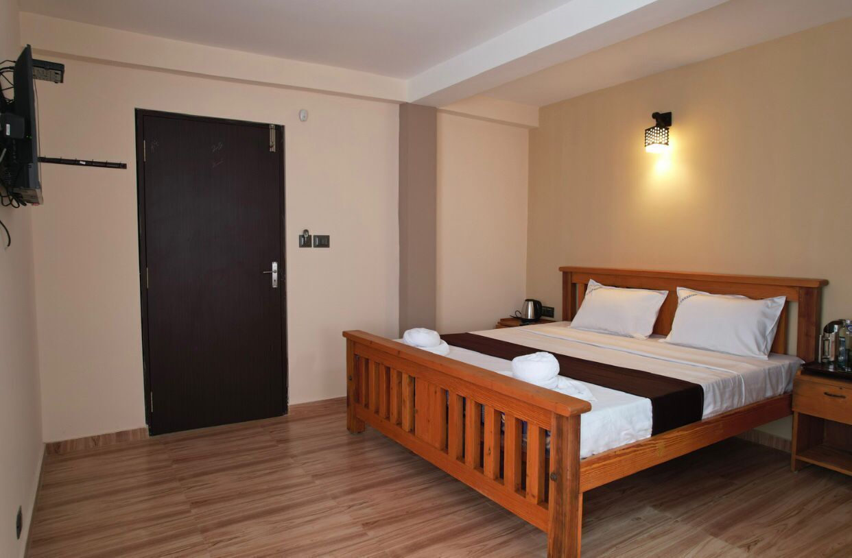 Une chambre à coucher avec un lit en bois, une table de chevet, une lampe fixée au mur et une porte.