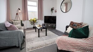 Ett vardagsrum med två soffor, ett soffbord, en tv och ett stort fönster med gardiner.