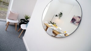 Ett modernt matområde med en rund spegel som reflekterar rummet, ett träbord dukat för två personer, en liten krukväxt och en stol med en kudde.