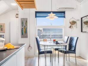 A modern kitchen with a dining area, featuring a round table with chairs, a hanging light fixture, and a view of the outside. - 4 Person Holiday Home in Hemmet (Hemmet)