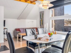 Een moderne eetruimte met een ronde tafel, zwarte lederen stoelen en een wit plafond met houten balken.