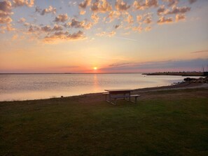A sunset over a calm body of water with a picnic table and grassy area. - 4 Person Holiday Home in Hemmet (Hemmet)