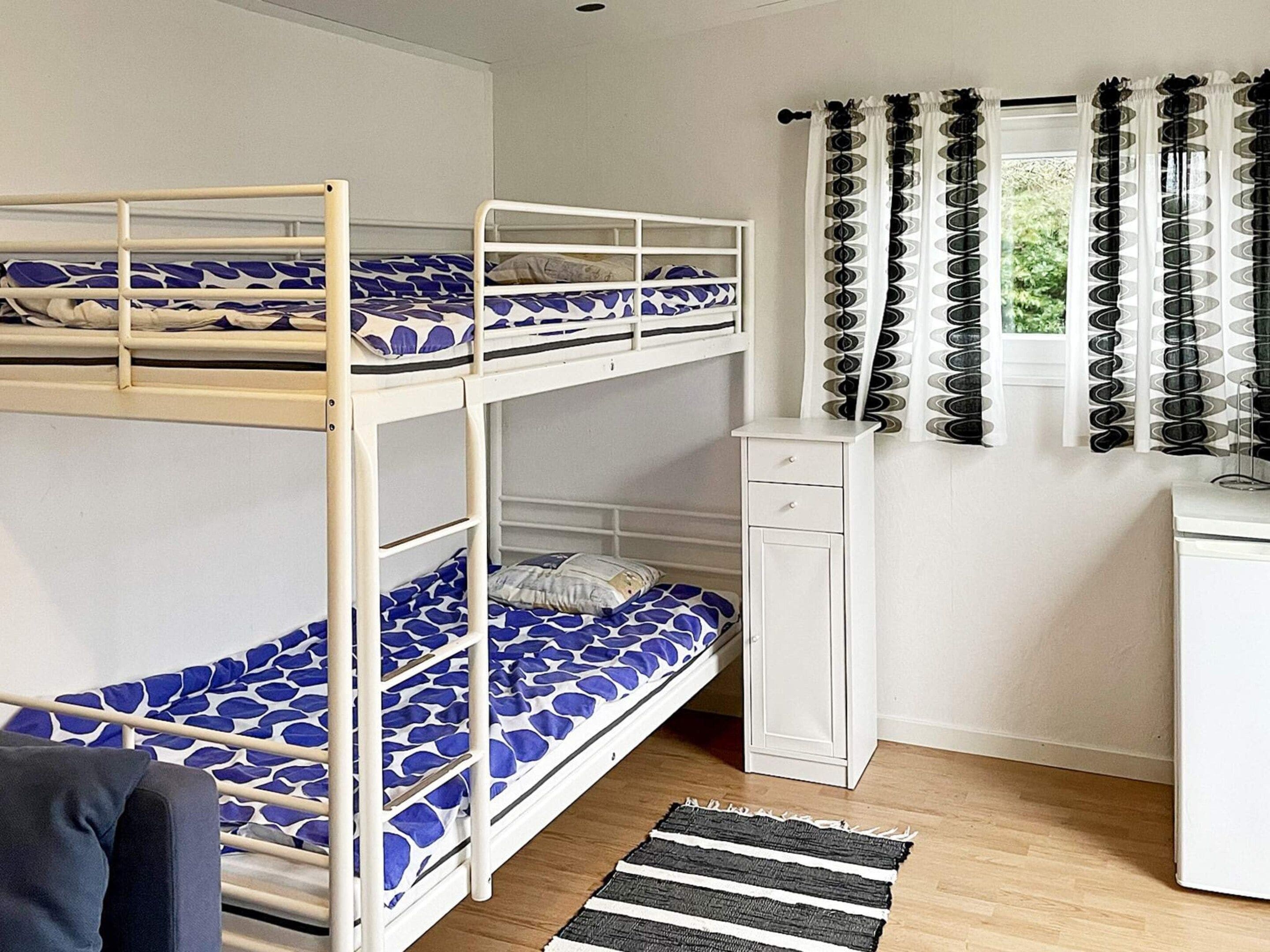 Quarto com beliche, escrivaninha e janela com cortinas.