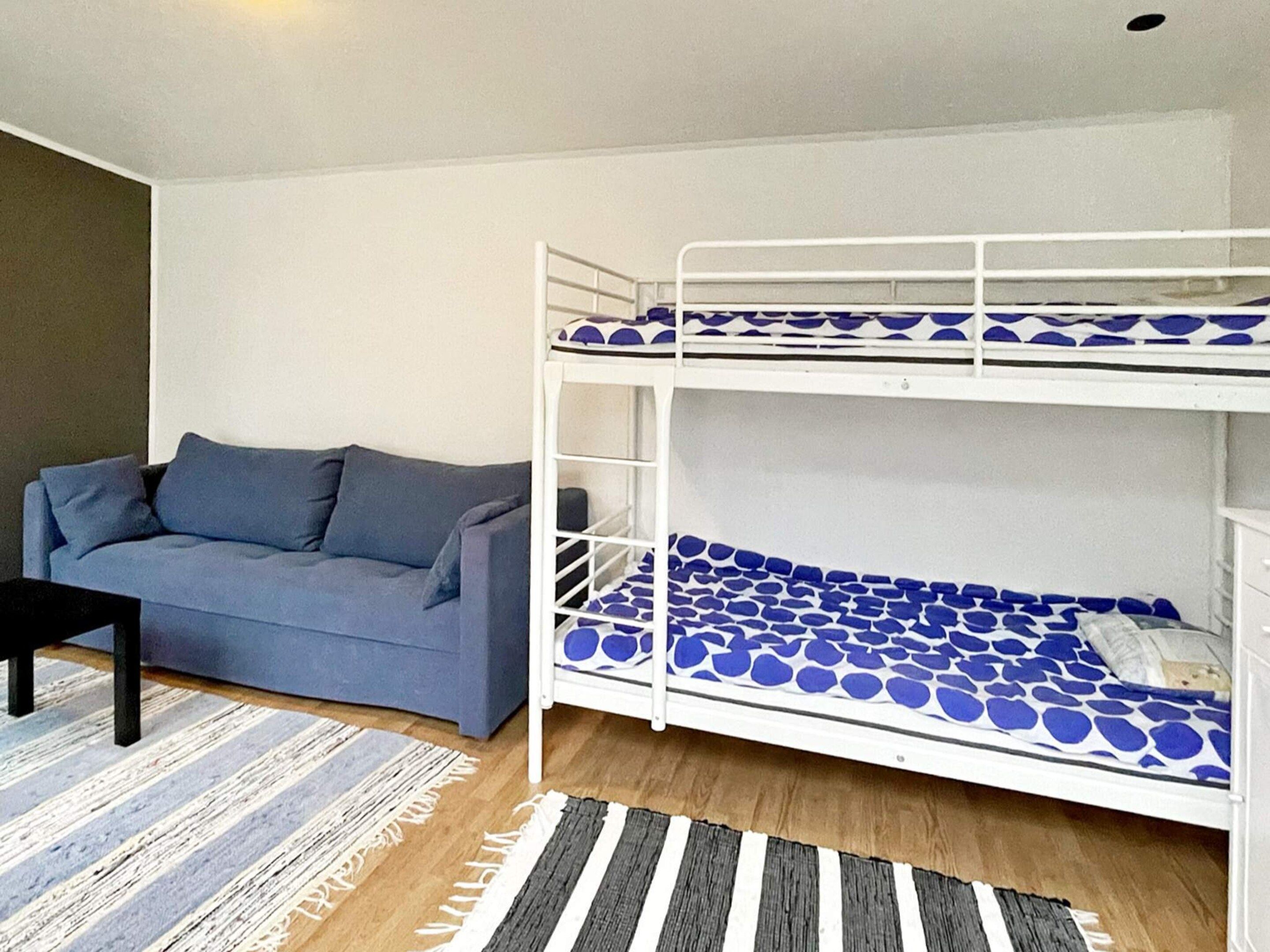 A bunk bed with a patterned mattress, a sofa with cushions, and a striped rug.