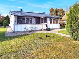 Une maison de plain-pied avec un porche abrité, une petite pelouse et un oiseau perché dans l’herbe.